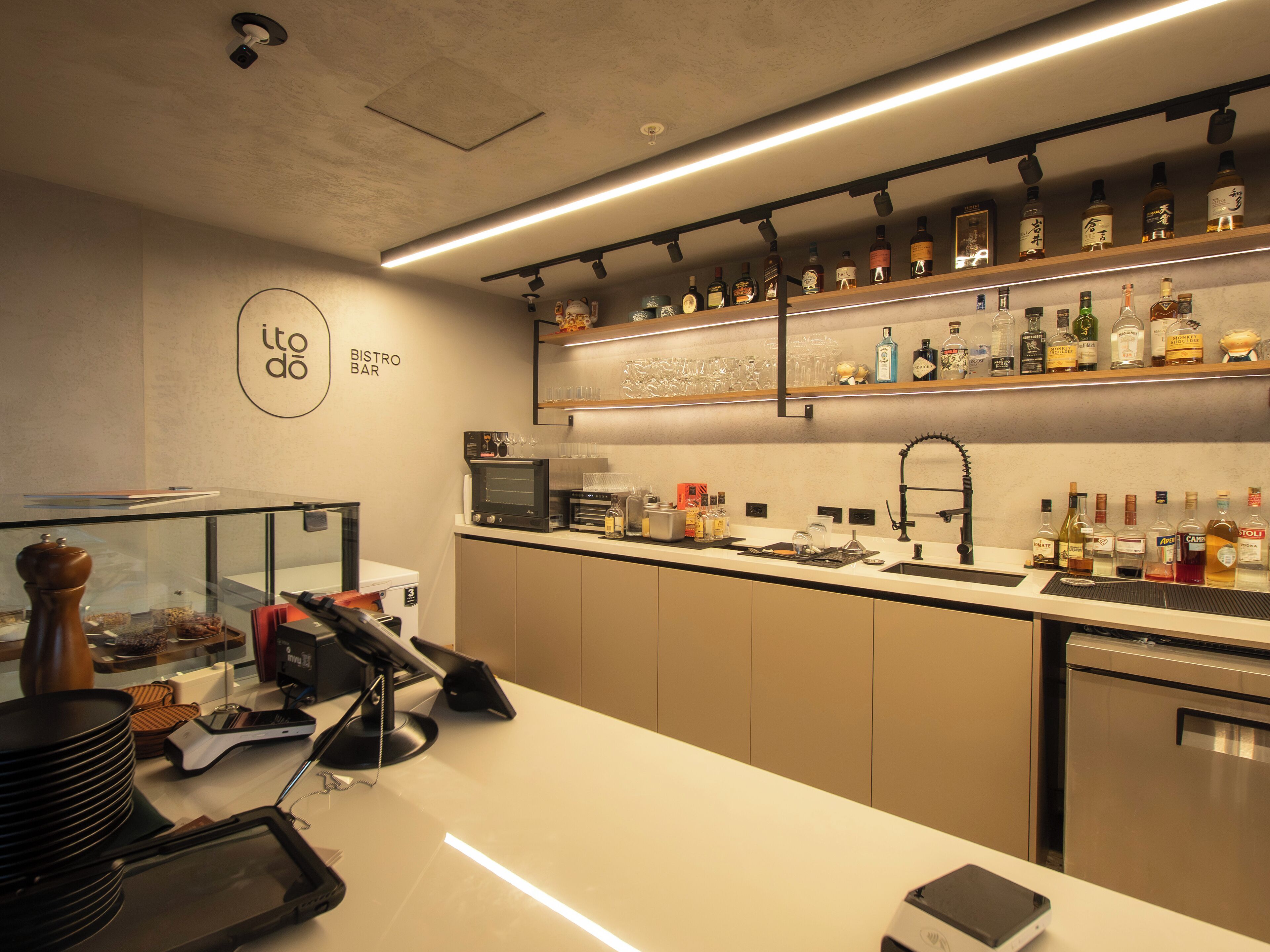 A modern bar area with a counter, shelves of liquor bottles, a coffee machine, and a glass display case.