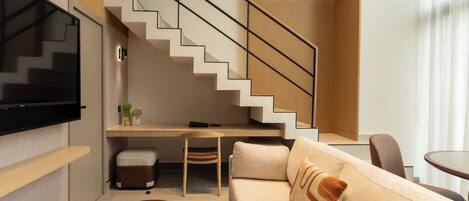 A modern living room with a staircase, a flat-screen TV, a desk, and a sofa.