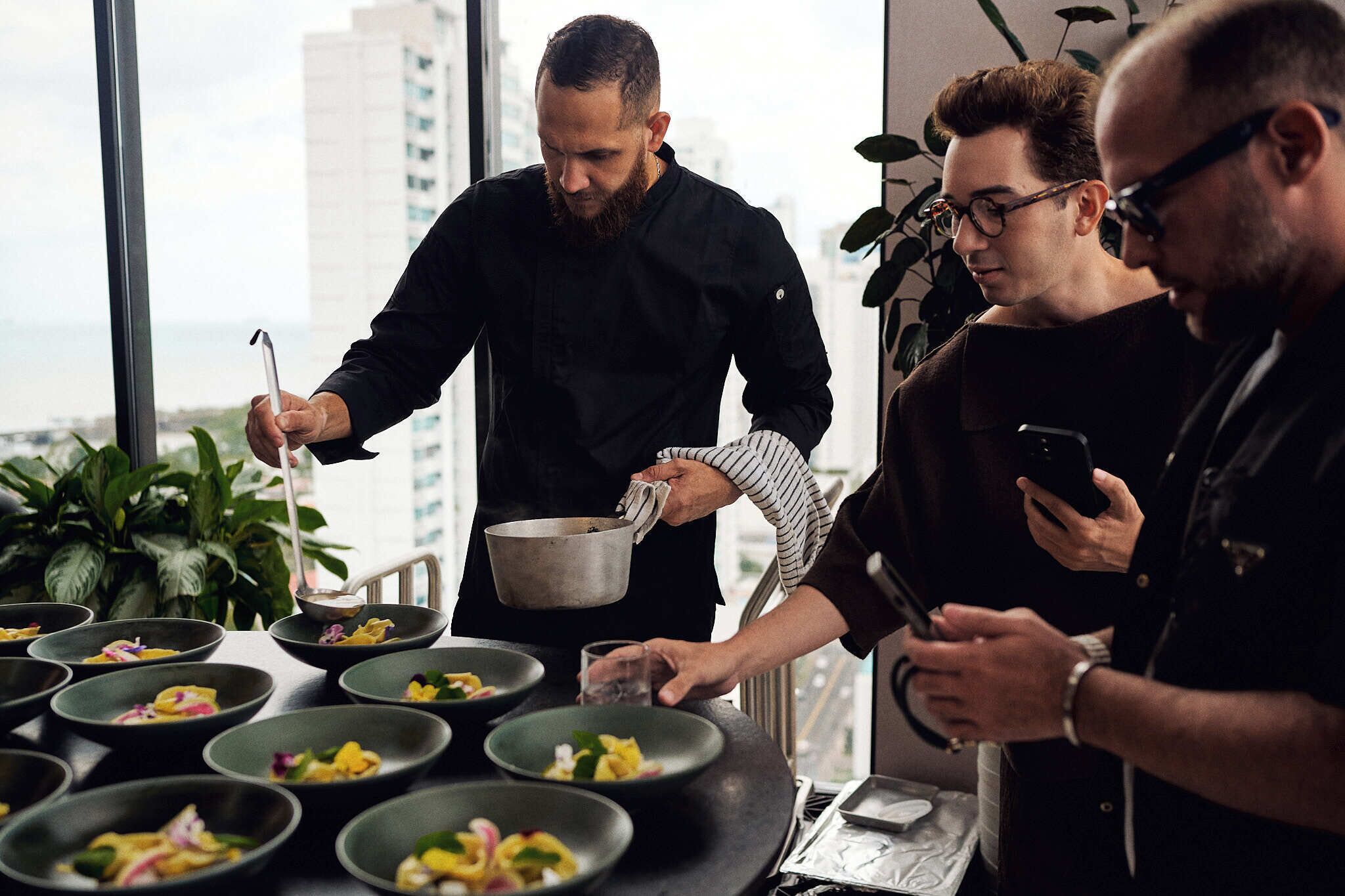 A group of people in a modern kitchen with a city view, preparing food.