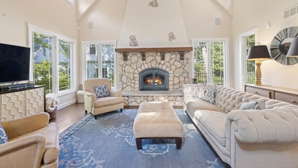 A spacious living room with a stone fireplace, large windows, and a high ceiling. - Grand Beach 4BR Pool House with Private Pool, Golf Cart & Fireplace (New Buffalo)
