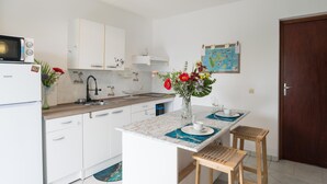 A compact kitchen with white cabinets, a microwave, a sink, and a small island with stools. There is a wooden door and a corkboard with a map on the wall.