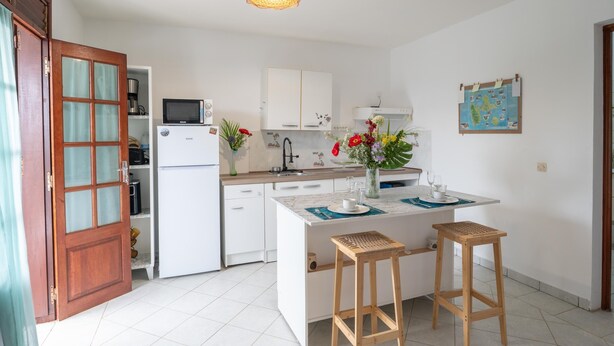 A compact kitchen with white cabinets, a microwave, and a sink. There are two wooden stools and a vase with flowers on the island.