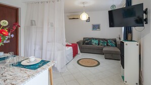 A living room with a sofa, a TV mounted on the wall, and a dining area with a table set for two.