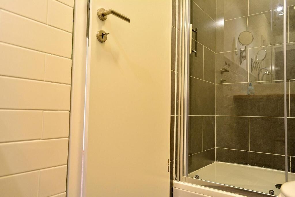 Un baño con cabina de ducha acristalada, paredes con azulejos blancos y una puerta con pomo.