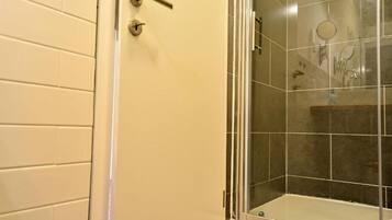 Un baño con cabina de ducha acristalada, paredes con azulejos blancos y una puerta con pomo.