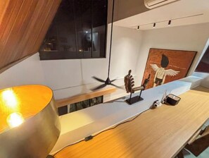 Une chambre moderne équipée d’un bureau, d’une lampe, d’un ventilateur de plafond et d’une œuvre d’art encadrée au mur.