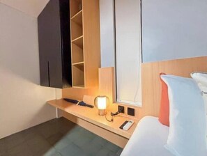 A hotel room with a bed, bedside table, lamp, and a built-in shelf with storage compartments.