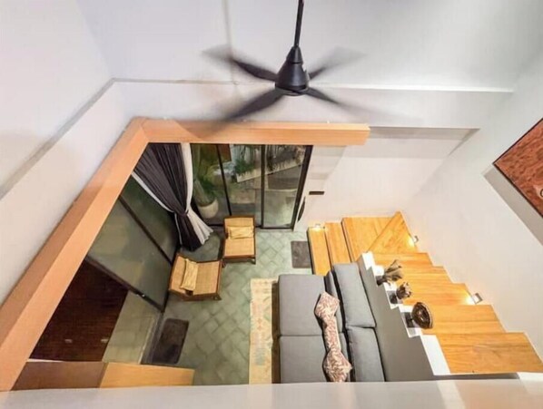 A modern loft-style room with a sloped ceiling, a ceiling fan, a built-in seating area with a sofa and a small table, and a view of the outdoors through a large window.