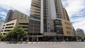 Un edificio a più piani con un design architettonico moderno, caratterizzato da un elemento verticale prominente e uno spazio commerciale a livello strada con insegna.