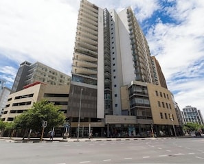 A multi-story building with a prominent vertical structure, a ground-level commercial space, and a clear sky.