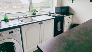 A kitchen with a washing machine, a sink, a microwave, and cabinets. - Comfy 3BR Flat on Quiet Street in Wollaton with FREE Parking (Nottingham)