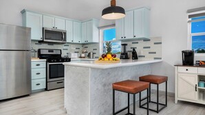 Een moderne keuken met lichtblauwe kastjes, roestvrijstalen apparatuur, een marmeren eiland en twee barkrukken.