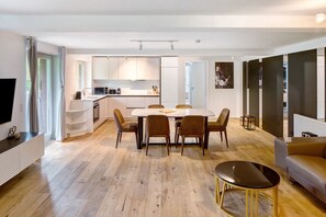 Una cocina moderna con armarios blancos, un comedor con mesa y sillas, un televisor y un sofá en la sala.