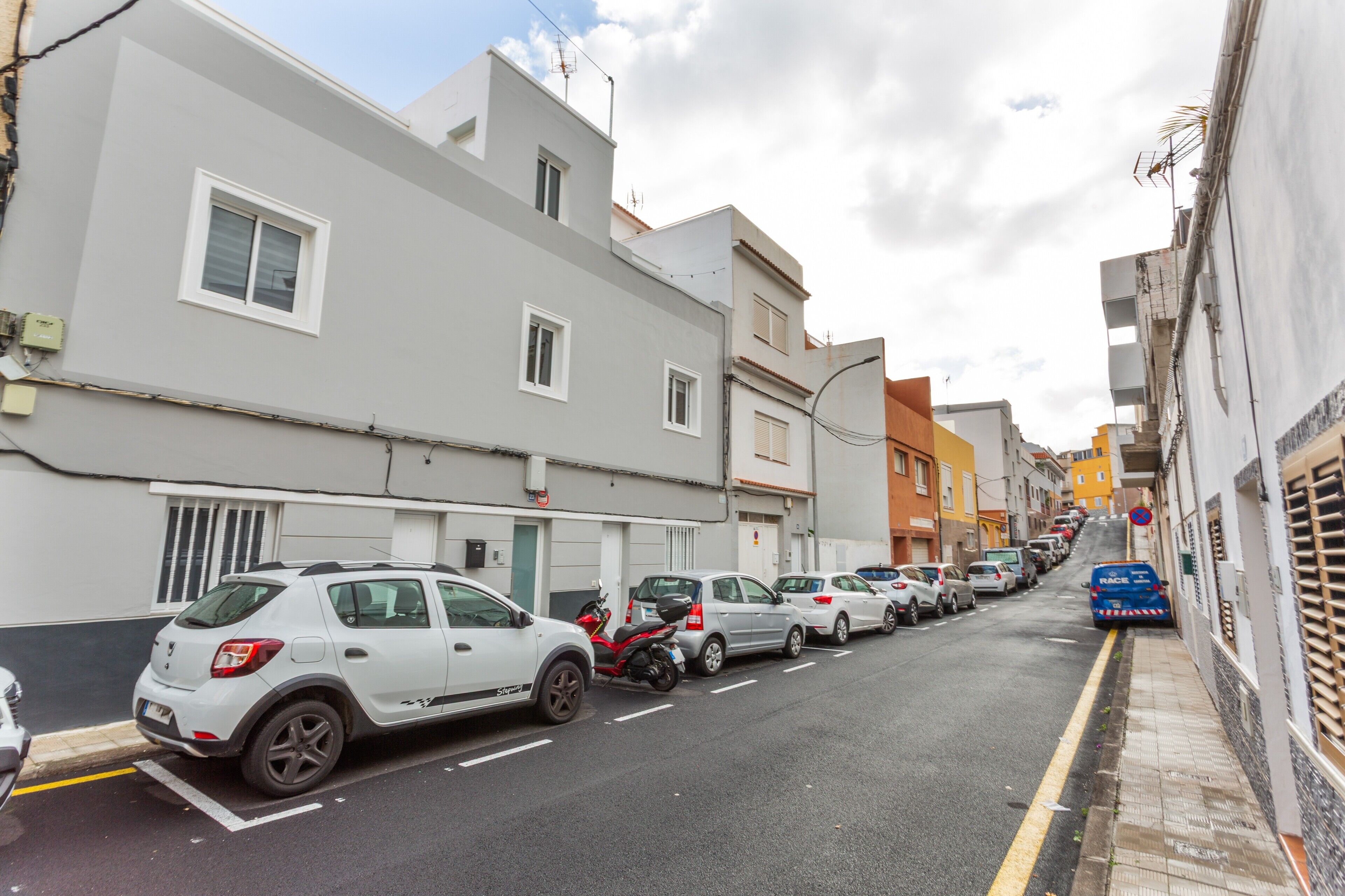 Eine schmale Stadtstraße gesäumt von parkenden Autos und Gebäuden.