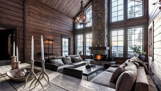 Interior acogedor de una cabaña de madera con chimenea, ventanas grandes y una zona de estar moderna.