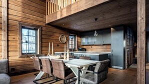 Un interior rústico de madera con comedor que incluye una mesa y sillas de madera, una cocina con electrodomésticos modernos y un ventanal que proporciona luz natural.