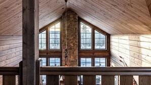 Una habitación con paredes de madera y un pilar de piedra, ventanas amplias y una barandilla de madera.