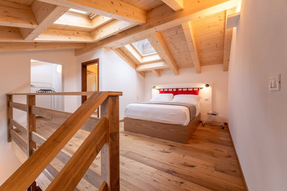 Quarto com cama de madeira, claraboia e escada de madeira.