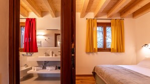 A bedroom with a bed, a window with yellow curtains, and a bathroom with a sink and mirror. - Villetta Rossa by Wonderful Italy (Bellagio)