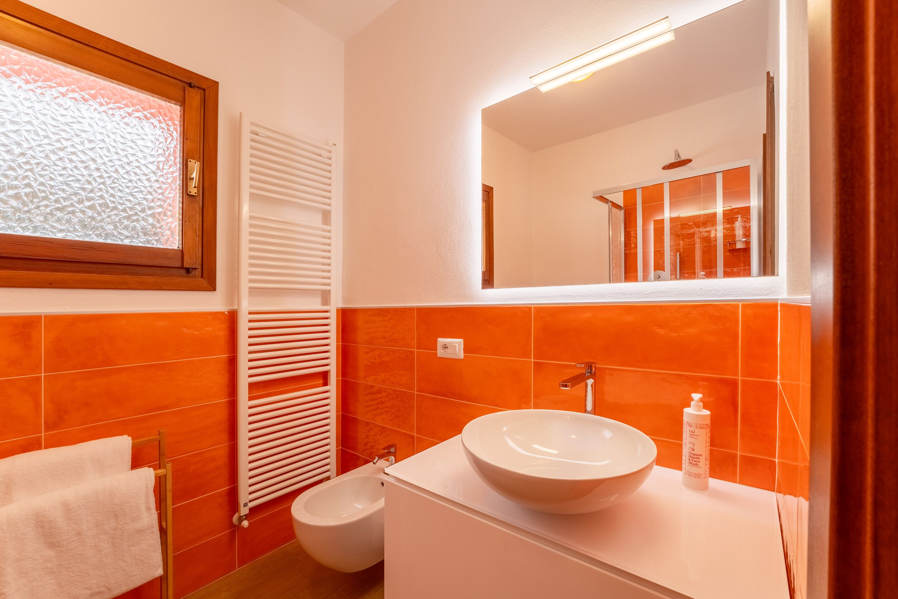 A bathroom with a white sink, a mirror, and orange tiles.