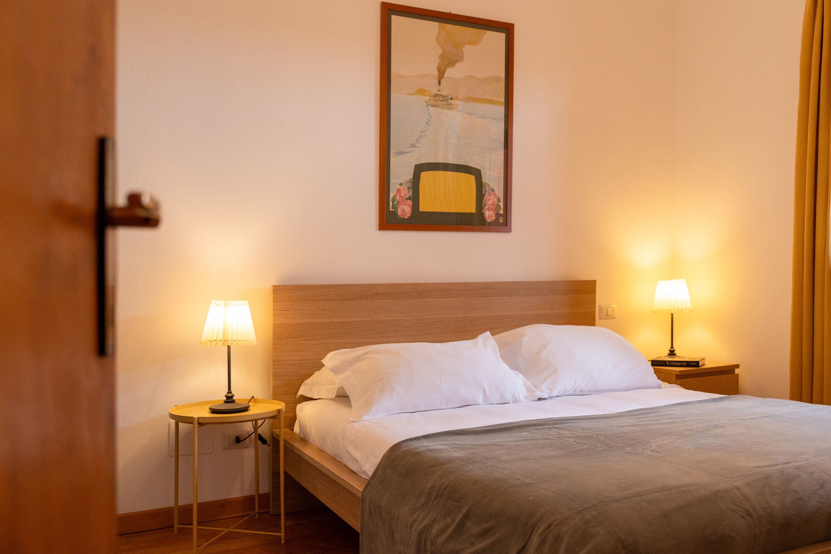 Een hotelkamer met een bed, twee bedlampen, een schilderij aan de muur en een deur.