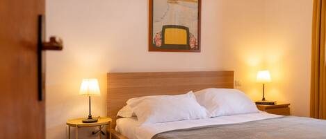 Een hotelkamer met een bed, twee bedlampen, een schilderij aan de muur en een deur.