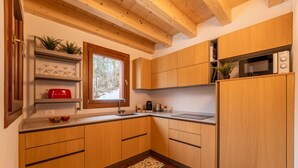 A modern kitchen with wooden cabinets, a built-in microwave, and a window with a view of trees. - Villetta Rossa by Wonderful Italy (Bellagio)