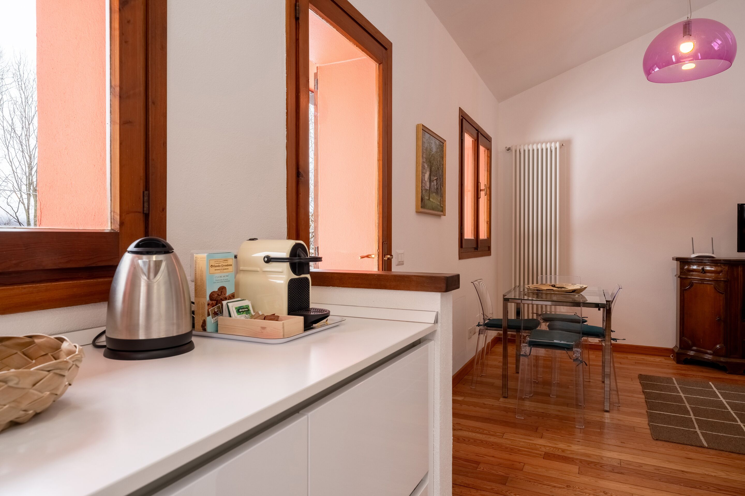 A kitchen with a kettle, toaster, and breakfast items on the counter. There is a dining table with chairs and a radiator in the background.