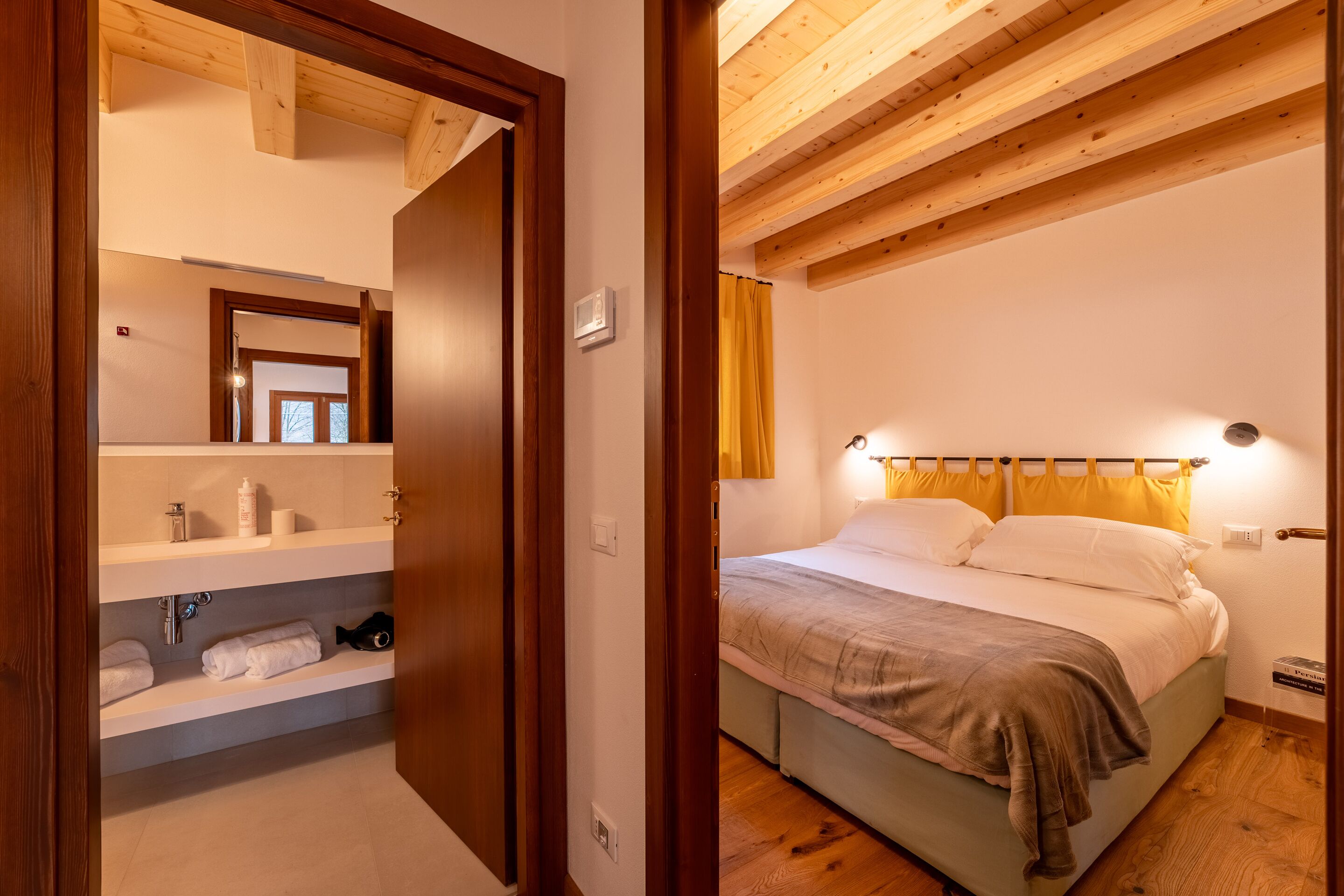 Une chambre à coucher avec un lit, une table de chevet et une commode. Le plafond est en bois et il y a une fenêtre avec des rideaux.