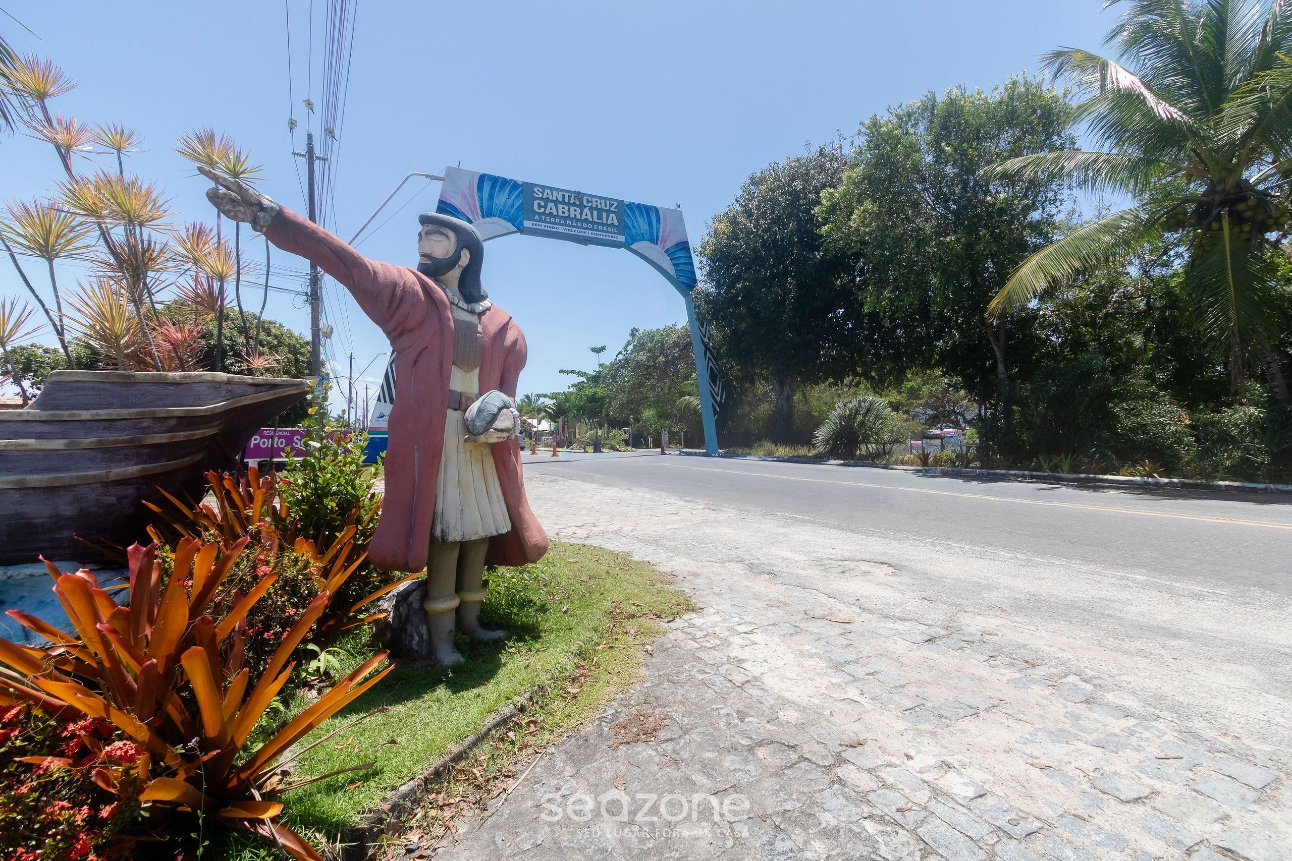 A statue with a sign reading "Santa Cruz Cabralia" and a road in the background.
