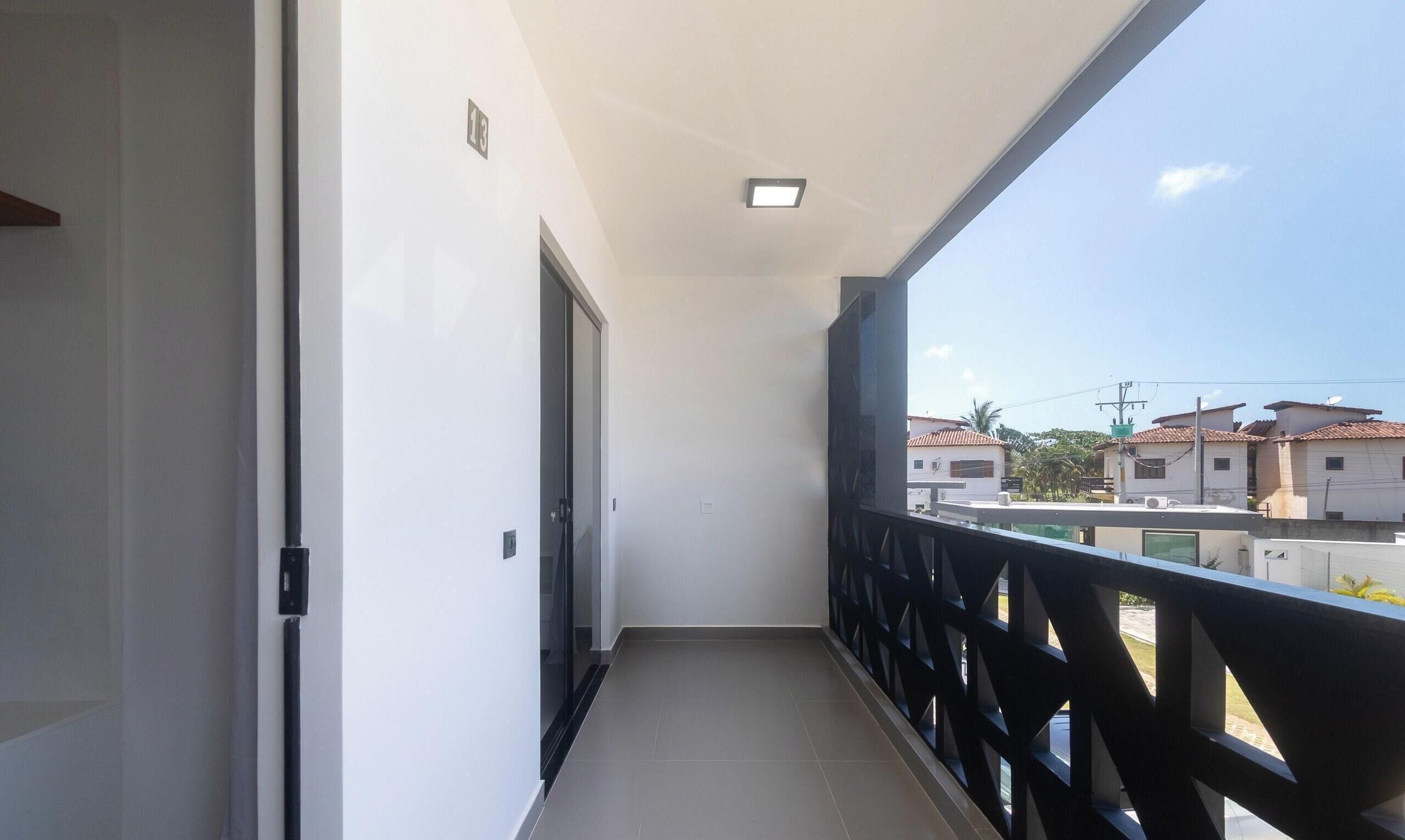 A narrow balcony with a black railing, a door on the left, and a clear view of buildings in the background.
