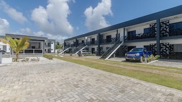 Ein modernes Gebäude mit einem gepflasterten Innenhof, mehreren Balkonen und einem blauen Auto vor der Fassade.