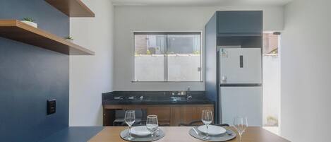 A modern kitchen with a dining table set for two, a built-in oven, and a refrigerator.