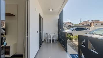 Ein schmaler Balkon mit Tisch und Stühlen, einer Schiebetür und im Hintergrund eine Aussicht auf parkende Autos und Gebäude.