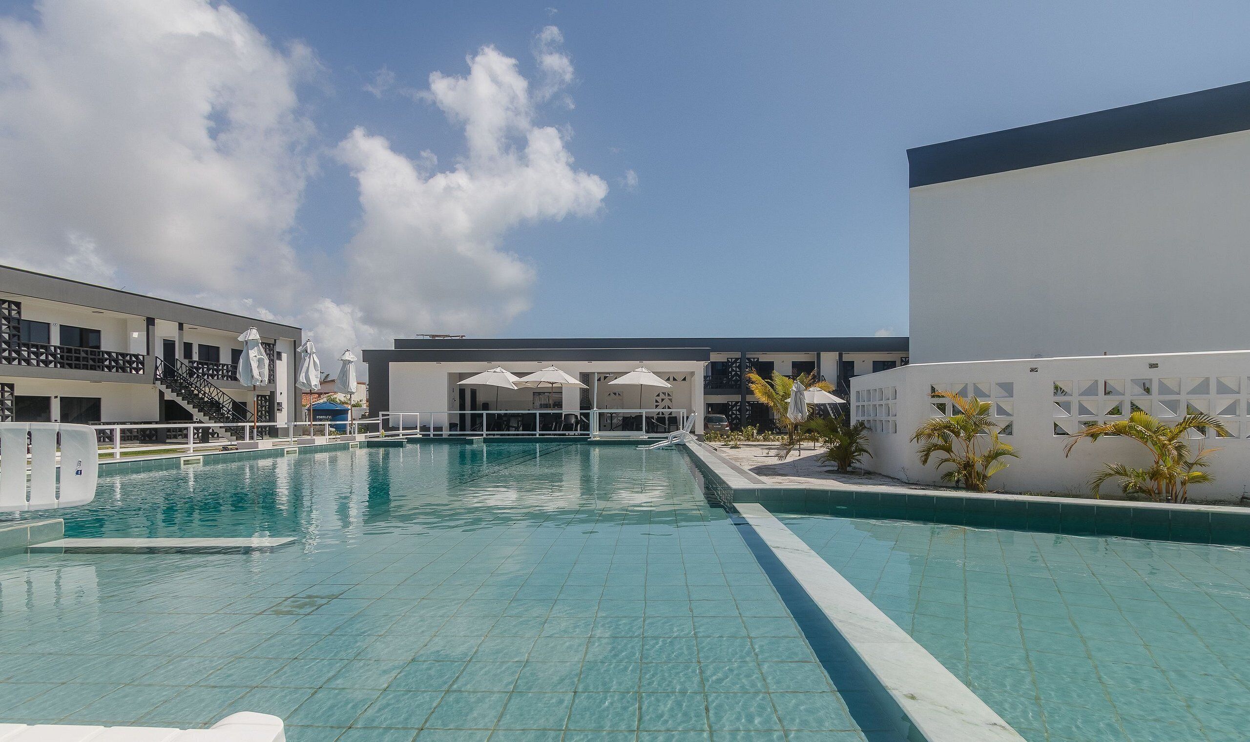 Ein Schwimmbecken mit klarem, blauem Wasser, umgeben von einem weißen Gebäude mit mehreren Fenstern und einem Balkon.