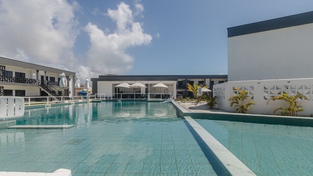 Una piscina con agua cristalina azul, rodeada por un edificio blanco con múltiples ventanas y un balcón.