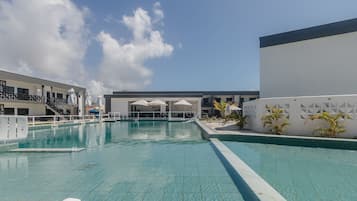 Ein Schwimmbecken mit klarem, blauem Wasser, umgeben von einem weißen Gebäude mit mehreren Fenstern und einem Balkon.