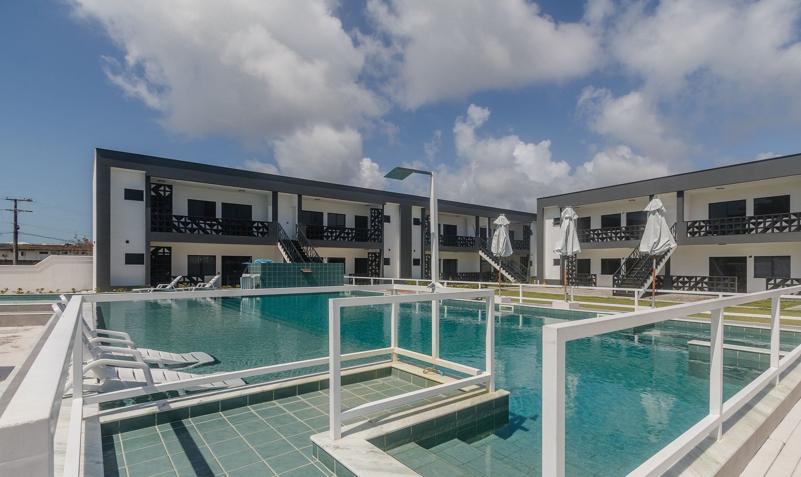 A modern hotel with a swimming pool, outdoor seating, and a clear blue sky.