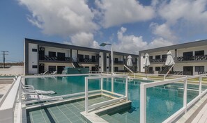 Un hôtel moderne doté d’une piscine, d’un espace extérieur aménagé et offrant une vue sur un ciel d’un bleu éclatant.