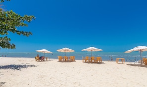 Une plage bordée de rangées de chaises jaunes et de parasols blancs, un ciel bleu dégagé et l’océan en toile de fond.