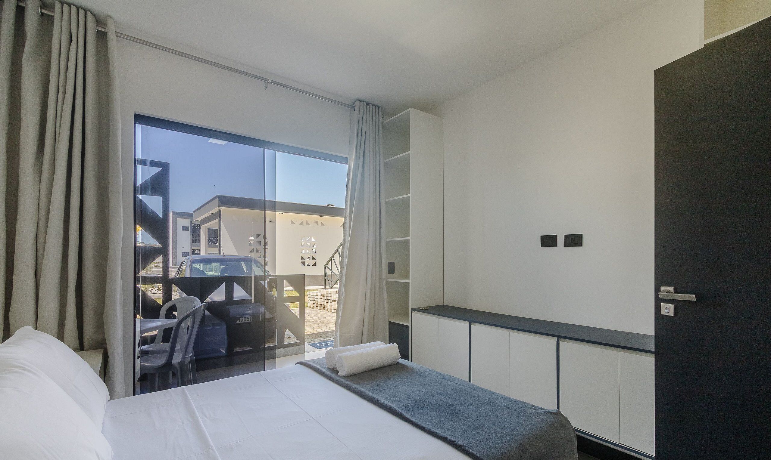 Ein Hotelzimmer mit einem Bett, einem kleinen Tisch, einer Sitzecke mit Stühlen, einem großen Fenster und Blick nach draußen.