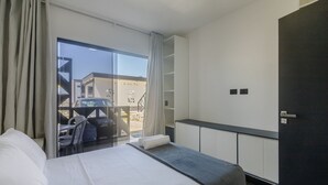 Una habitación de hotel con cama, una mesita, una zona de estar con sillas, un ventanal y vistas al exterior.