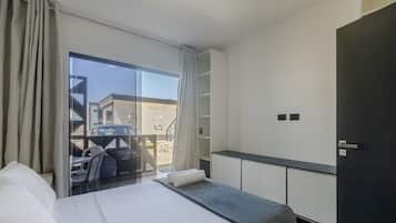 Ein Hotelzimmer mit einem Bett, einem kleinen Tisch, einer Sitzecke mit Stühlen, einem großen Fenster und Blick nach draußen.