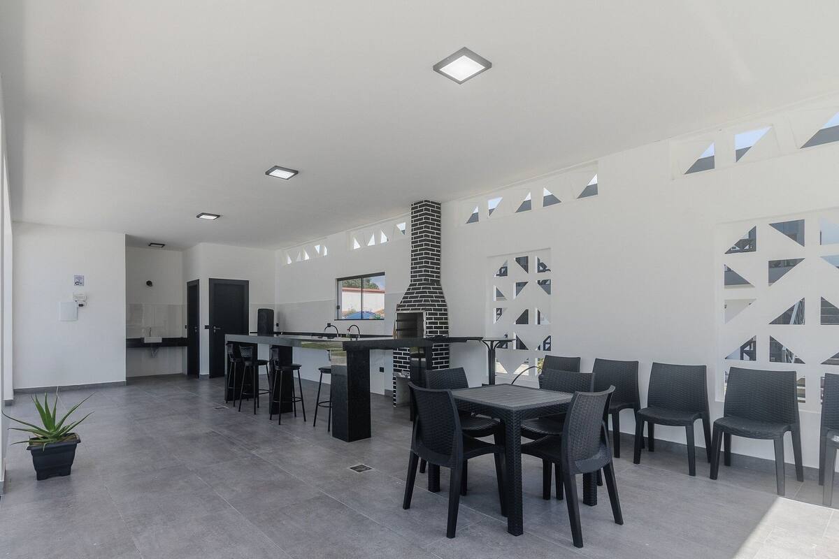 A modern outdoor dining area with a brick-built grill, black chairs, and a white interior.