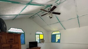 A bedroom with a bed, wooden wardrobe, TV, and a ceiling fan.