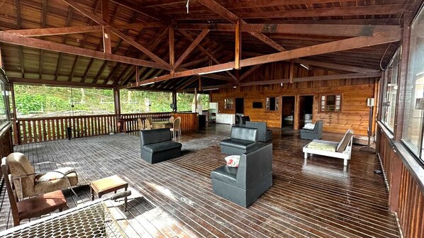 A covered outdoor deck with wooden flooring, seating areas, and large windows. - Pousada Canto da Montanha Guarujá (Guarujá)