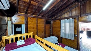 A cabin with two wooden beds, a ceiling fan, and a window with curtains. - Pousada Canto da Montanha Guarujá (Guarujá)