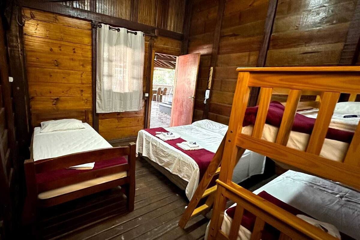Una habitación tipo cabaña con dos literas de madera, una mesita pequeña y una ventana con cortinas.