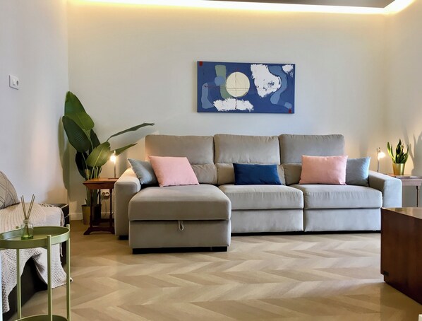 A modern living room with a grey sofa, a large abstract painting, and a green plant.