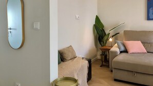 Un salon avec un canapé beige, une petite table sur laquelle est posée une plante, et un miroir fixé au mur.